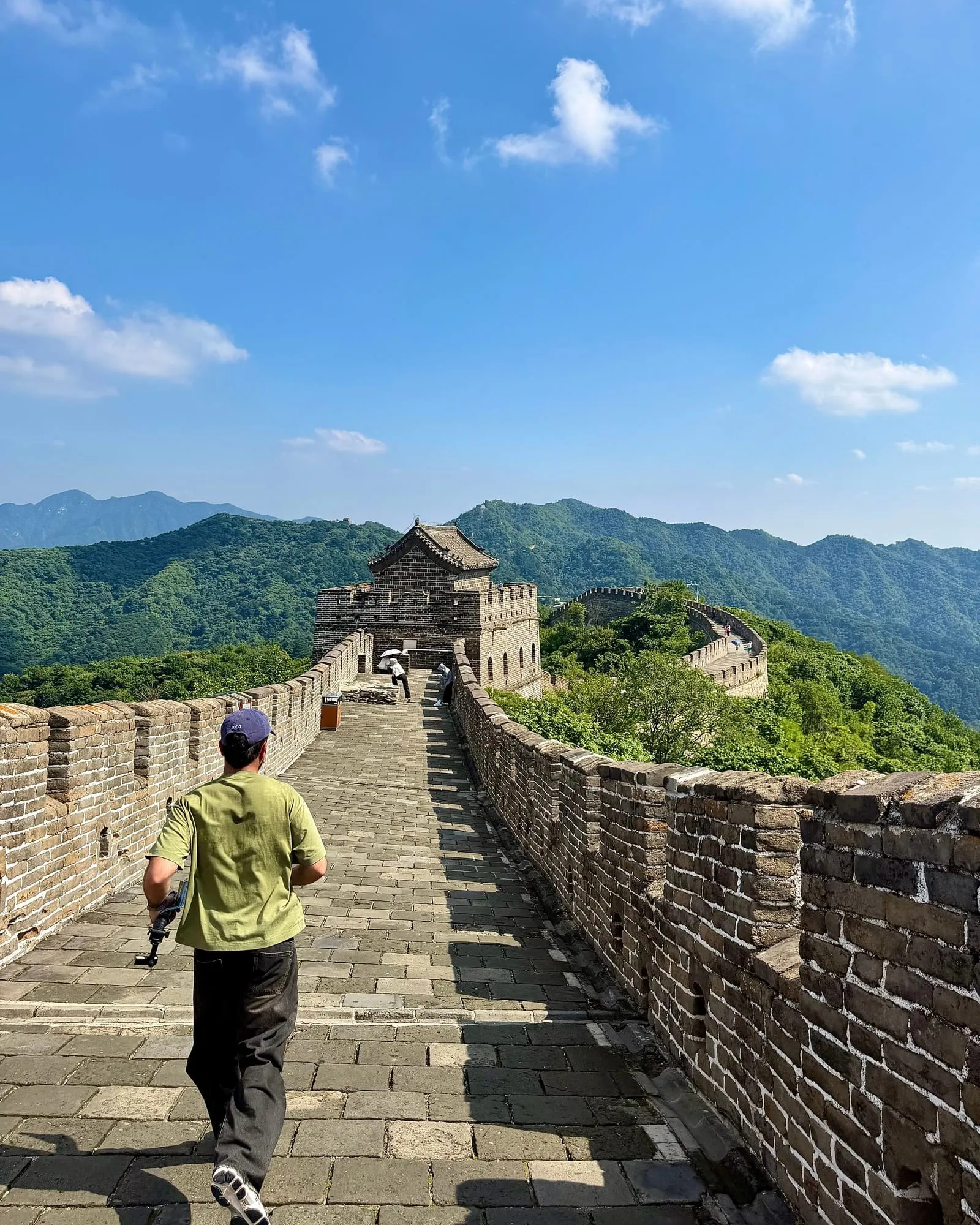 Un compagnon de route avance sur la Grande Muraille vers une tour de guet, sous un ciel bleu.