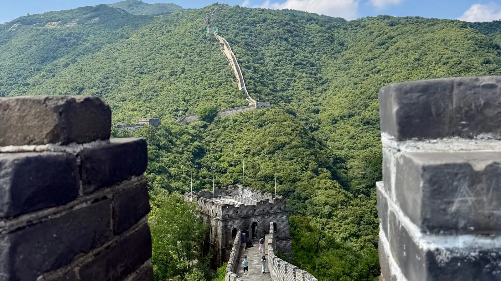 La Grande Muraille vue entre deux créneaux, avec une tour de guet et les collines de Mutianyu.